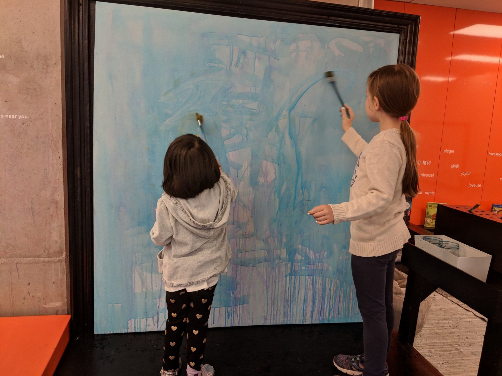 Two girls painting at large canvas.