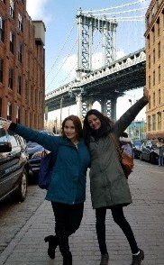 Two smiling women on city street with bridge in the background