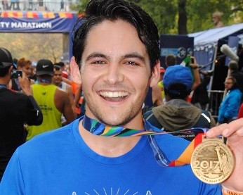 Tom Schrank (School of Professional Studies) after finishing the NYC Marathon. Smiling man holding gold medal.
