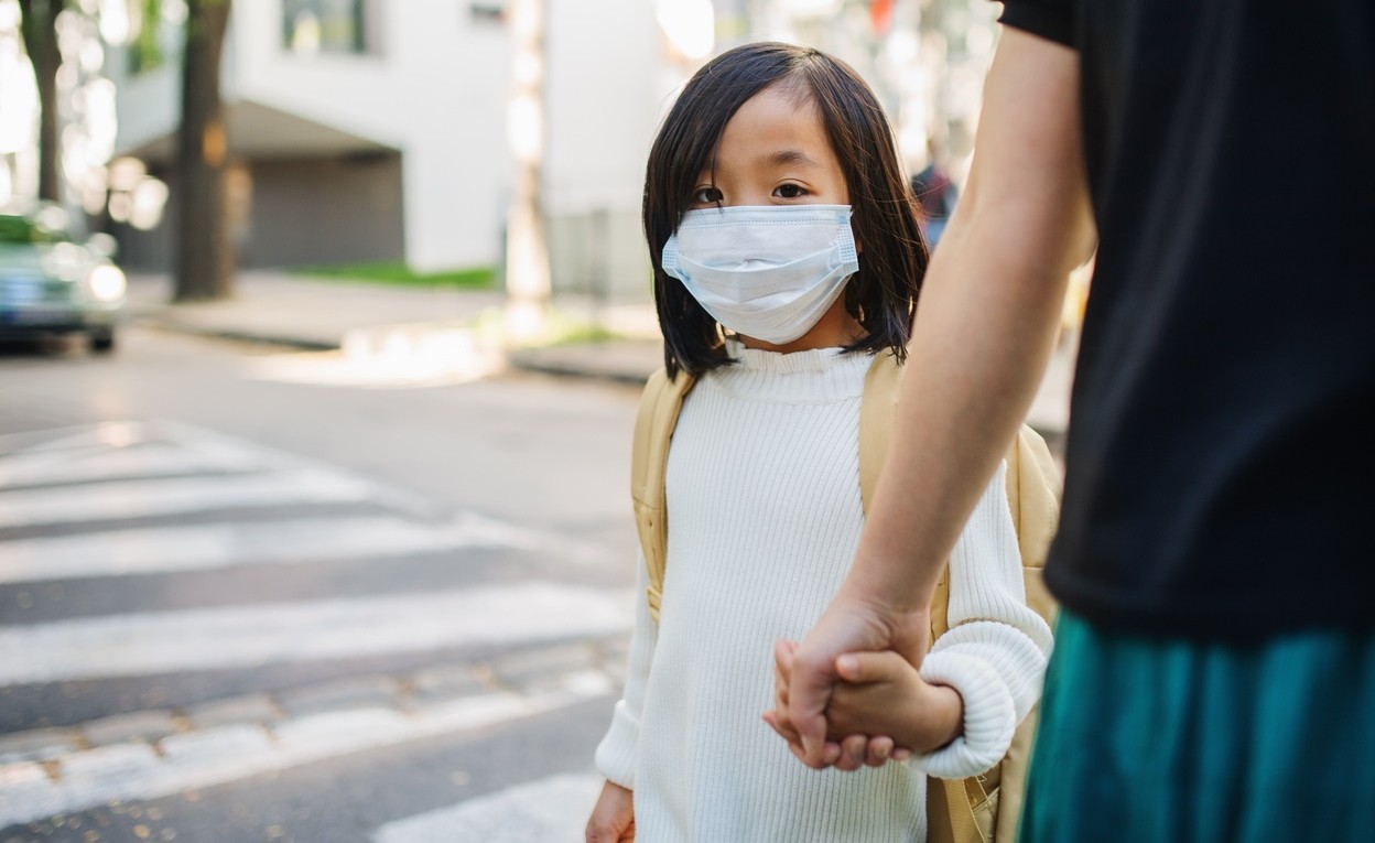 Girl with mask crossing street holding and adult's hand.