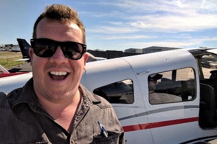 Benjamin Royce (School of Professional Studies) working on his private pilot's license. Smiling man in sunglasses in front of plane.